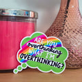 Pink candle and decorative vase with a rose on a wooden surface, accompanied by a colorful sticker.