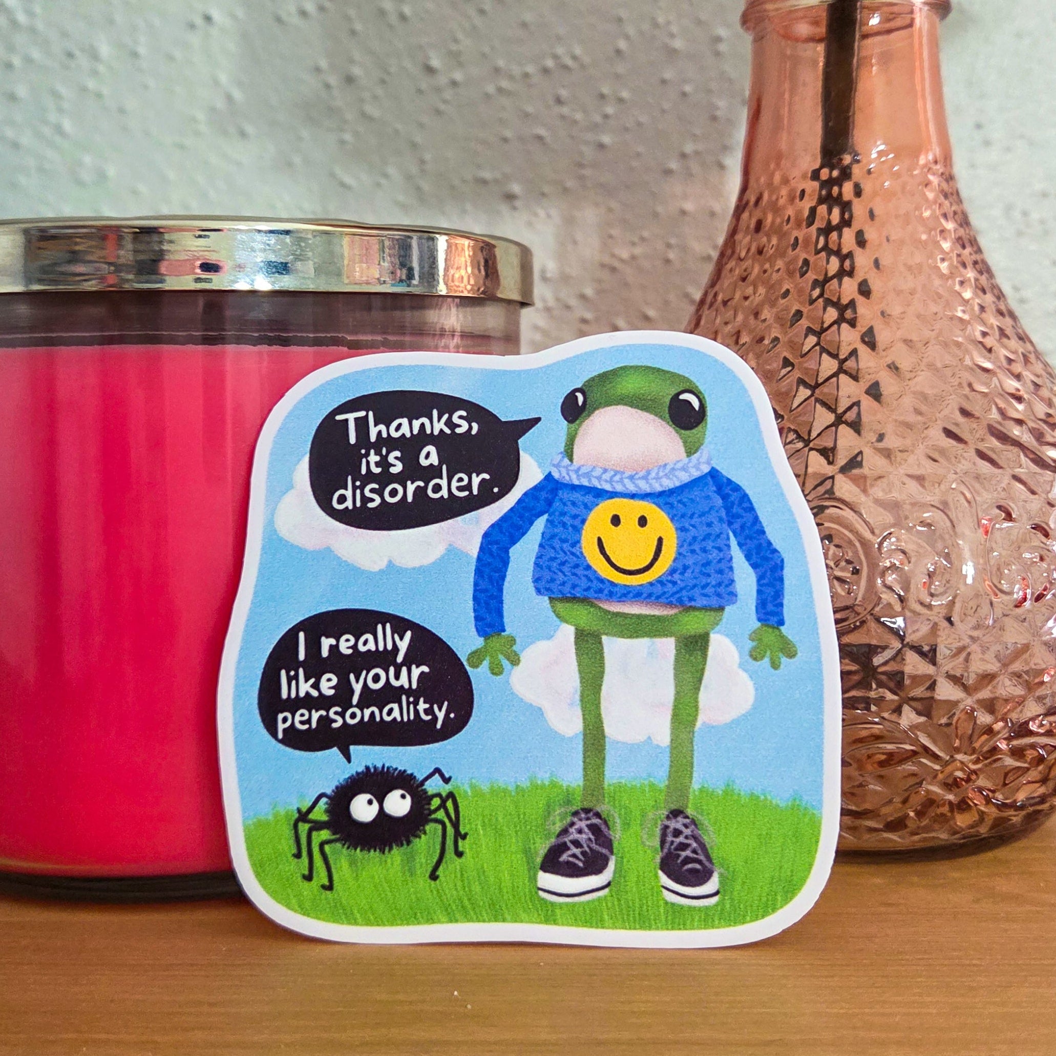 Sticker with a cartoon character and text on a pink candle and vase with flowers.