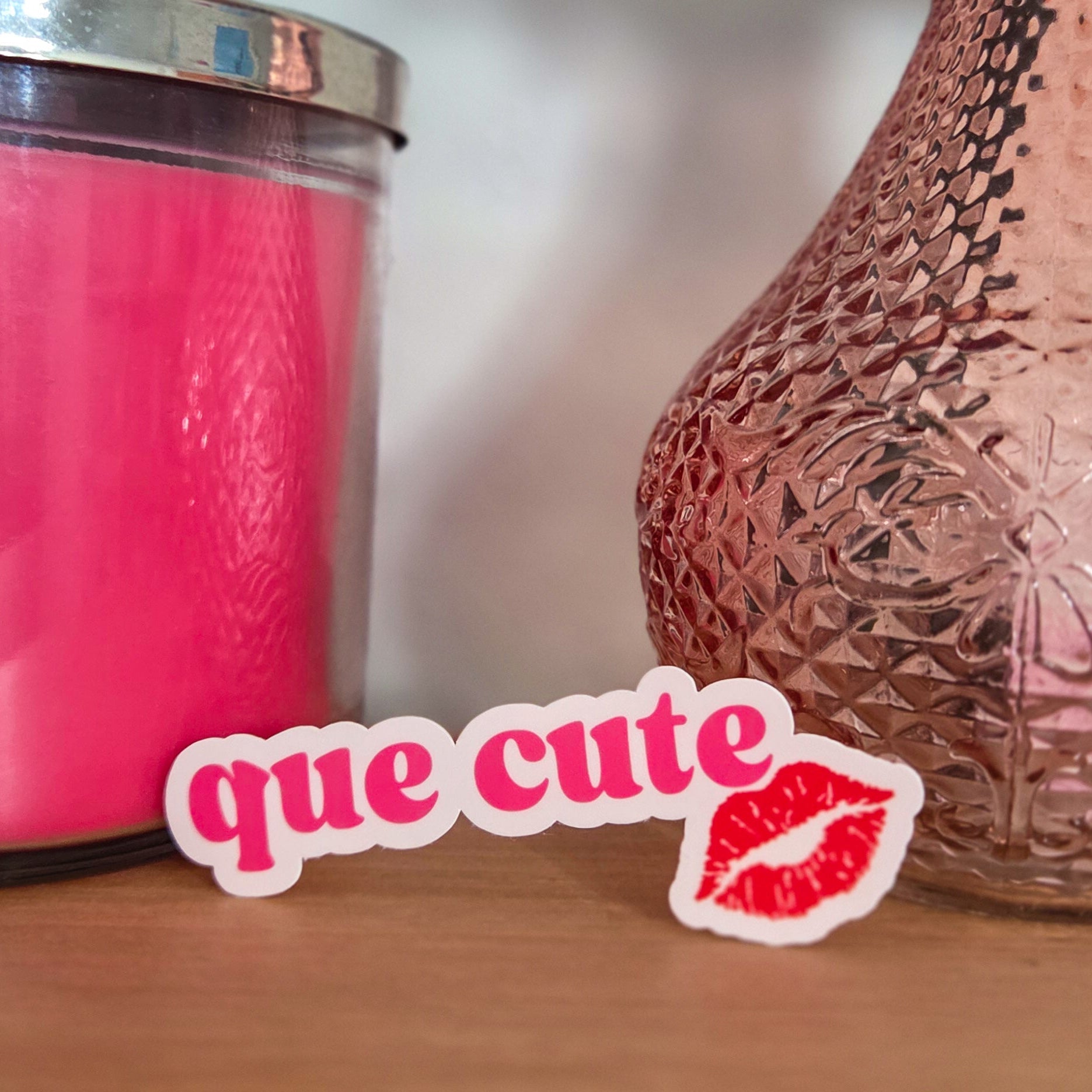 Rose gold textured vase on a wooden surface with a pink candle and 'que cute' sticker.