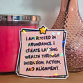 Pink candle and vase with a motivational quote sticker on a wooden surface.