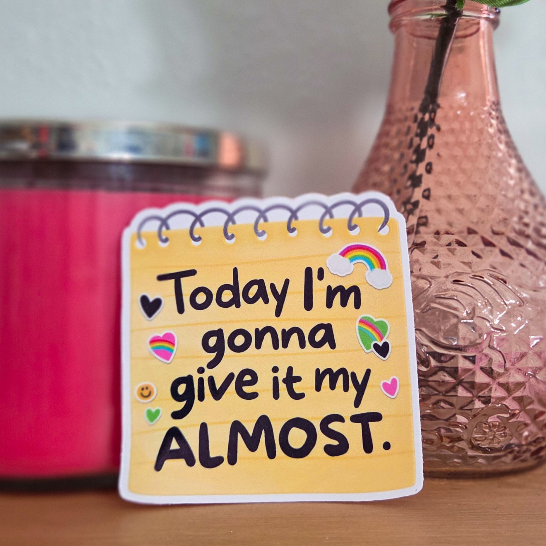 Note with 'Today I'm gonna give it my Almost' text on a wooden surface with a pink candle and vase in the background.