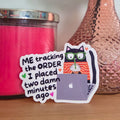 Pink candle, pink vase with a flower, and a sticker on a wooden surface.