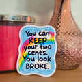 Colorful sticker with text on a wooden surface with a pink candle and vase in the background.